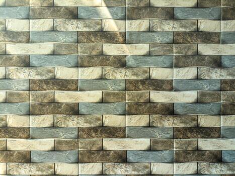 Textured stone wall with interlocking rectangular tiles in beige, brown, and gray hues, creating a modern and elegant design with light and shadow play photo