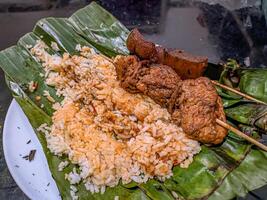 Indonesian grilled rice nasi bakar with cow nose skewers and marinated tofu skewers, served on banana leaves, showcasing traditional street food photo