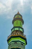 Green and gold minaret tower against a clear blue sky with wispy clouds, Islamic architecture, religious symbol photo