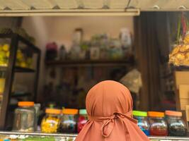 Back view of a person in a hijab looking at a vibrant street market stall filled with various items, highlighting local culture and commerce photo