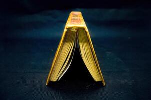 Open Quran book with golden edges on dark background, showcasing intricate Arabic script, symbolizing Islamic faith and spirituality photo