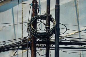 Urban chaos depicted through tangled electrical wires against a building and clear blue sky, showcasing complex city infrastructure photo