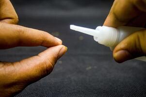 Close up of hands applying cyanoacrylate ethyl adhesive, showcasing precision and strength. Ideal for DIY projects, repairs, and crafts. The focus is on the nozzle and a drop of glue photo