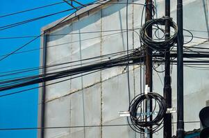Urban chaos depicted through tangled electrical wires against a building and clear blue sky, showcasing complex city infrastructure photo
