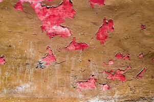 Close up of a wall with peeling red paint, revealing rough brown textures underneath. This image highlights the contrast between vibrant red and earthy brown, depicting decay and vintage appeal. photo