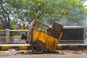 Overturned yellow garbage cart on urban roadside with scattered trash and rising dust, depicting waste management issues photo
