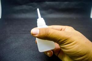 Hand holding a bottle of Cyanoacrylate Ethyl adhesive with a precision applicator tip against a dark background. Ideal for detailed adhesive work in DIY projects, crafts, and repairs photo