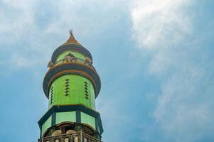 Green and gold minaret tower against a clear blue sky with wispy clouds, Islamic architecture, religious symbol photo