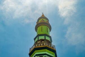 Green and gold minaret tower against a clear blue sky with wispy clouds, Islamic architecture, religious symbol photo