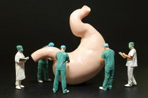 Miniature surgeons in scrubs performing an operation on a large model of a human stomach. photo