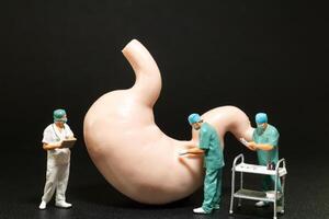 Miniature surgeons in scrubs performing an operation on a large model of a human stomach. photo