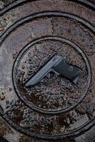 lack handgun on a wet, textured surface, emphasizing contrast between the matte finish of the firearm and the glistening puddles. Ideal for safety, tactical, or firearm-themed content. photo