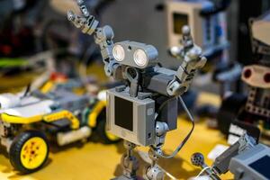 Detailed view of a toy humanoid robot built from construction blocks, with blurred robotics parts in the back photo
