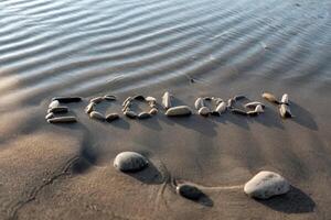 Stones arranged to spell 'Ecology' on a serene beach by rippling water. photo