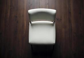 Modern white chair on dark wooden floor, viewed from above. photo