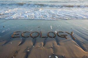 Ecology written in stones on a sandy beach with waves in the background. photo
