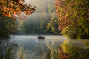 A small boat on a serene, misty lake surrounded by colorful autumn trees. photo
