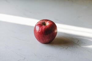 Single red apple on a white marble surface with natural light. photo
