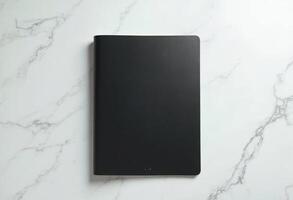 Sleek black hardcover notebook on a white marble surface. photo