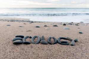 The word 'ecology' spelled with rocks on a sandy beach near the ocean waves. photo