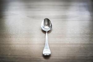 Single silver spoon on a wooden table, reflecting natural light. photo