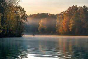 Serene autumn morning with lone figure fishing on a misty lake. photo