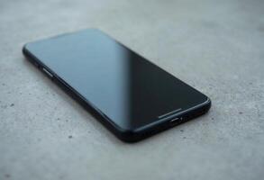 Close-up of a sleek black smartphone on a gray concrete surface. photo