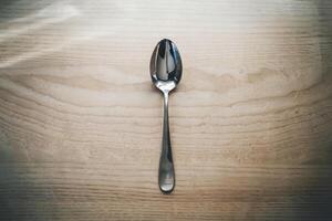 A single metal spoon on a wooden surface under natural lighting. photo