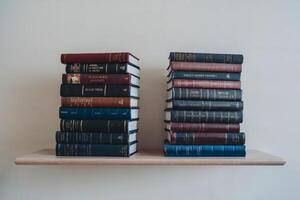 Stacked vintage books on a minimalist wooden shelf against a plain wall. photo
