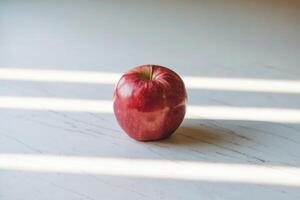 A fresh red apple rests on a marble surface with sunlight streaming in. photo