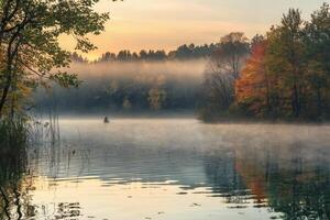 Lone figure kayaking on misty lake during sunrise in autumn. photo