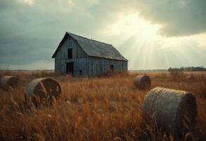 Old barn in a rural field with hay bales under a moody sky. photo