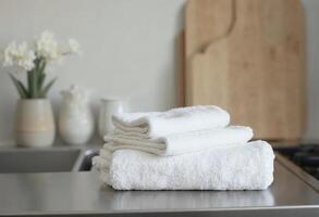 Neatly folded white towels on kitchen counter with wooden cutting board background. photo