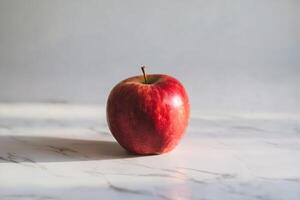 A fresh red apple sits on a marble surface, bathed in natural light. photo