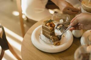 A hand holds a spoon, ready to enjoy a slice of cake with macadamia topping, capturing the cozy vibe of a cafe. photo
