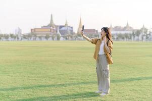 Traveler asian woman in her 30s take a livestream on smartphone while explores Wat Phra Kaew emerald Buddha. Share the wonders of Thai heritage through her journey. photo