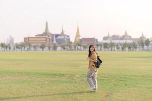 Traveler asian woman in her 30s, backpack slung over her shoulder, explores Wat Pra Kaew with childlike wonder. Sunlight dances on the golden rooftops, and a carefree smile photo