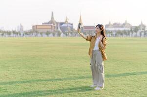 Traveler asian woman in her 30s take a livestream on smartphone while explores Wat Phra Kaew emerald Buddha. Share the wonders of Thai heritage through her journey. photo
