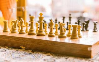 Chessboard with white chess pieces set up ready for play and black pieces blurred in background chess concept photo