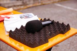 Microphone placed on soundproof foam, outdoor table setting, black and orange color contrast, interview preparation, broadcasting concept photo