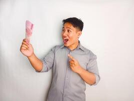 Young Asian rise up his hand while holding banknotes and shows happy expression wearing grey shirt isolated on white background photo