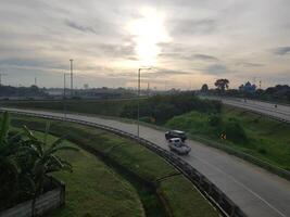 A car driving down a highway with the sun setting behind it photo