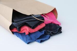 A paper bag filled with colorful clothes. Concept of consumption, second-hand, recycling, charity. A purchase in a thrift store. Environmental issue of overconsumption photo