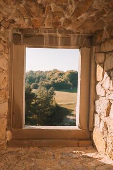 Scenic view through a narrow square open window in a Castle Bobolice looking over green fields in the valley in the south of Poland. photo