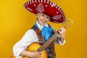 portrait of a happy middle aged woman smiling in front of a yellow background enjoying playing guitar dressed as a Mexican mariachi with sombrero photo