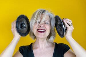 portrait of a beautifulscreaming middle-aged woman in front of a yellow background enjoying listening to loud music with speakers photo