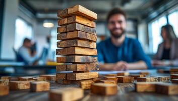 A man is sitting at a desk with a stack of wooden blocks in front of him. The blocks are arranged in a pyramid shape, and the man is smiling. Concept of playfulness and creativity photo