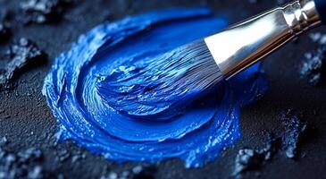 Bright blue paint applied with a brush on canvas. A vibrant blue paint is being mixed on a dark surface using a brush, showcasing the texture and color contrast vividly. photo