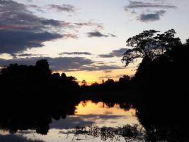 A sunset over a lake with trees and water photo