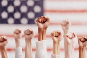 Hands with raised fists show solidarity and unity in front of a blurred American flag, symbolizing strength, activism, and diversity. photo